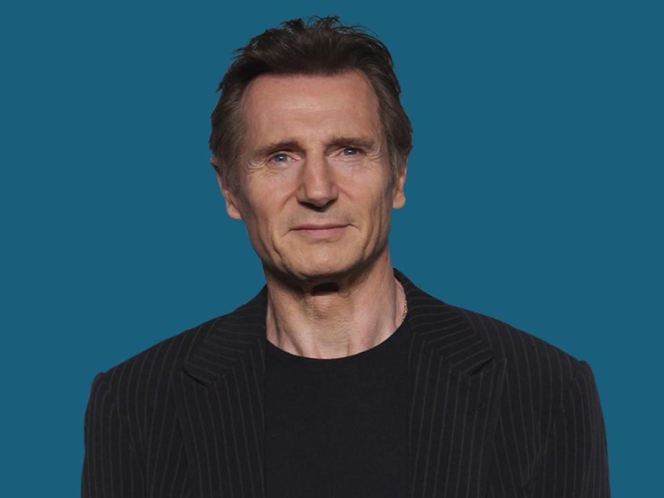 Liam Neeson poses against a turquoise background