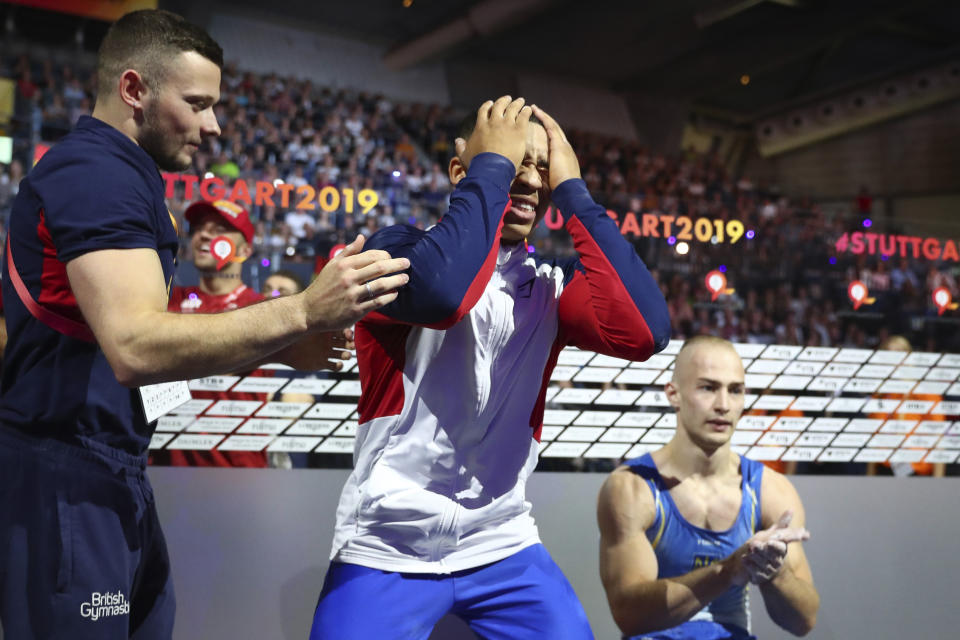 Gold medalist Joe Fraser of Great Britain, center, celebrates after his performance on the parallel bars in the men's apparatus finals at the Gymnastics World Championships in Stuttgart, Germany, Sunday, Oct. 13, 2019. (AP Photo/Matthias Schrader)