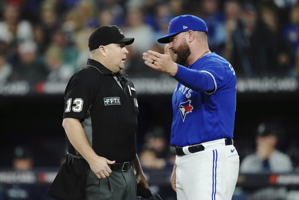 Toronto Blue Jays interim manager John Schneider talks with home plate umpire Todd Tichenor (13) during the fifth inning of Game 2 of the baseball team's AL wild-card playoff series against the Seattle Mariners on Saturday, Oct. 8, 2022, in Toronto. (Nathan Denette/The Canadian Press via AP)