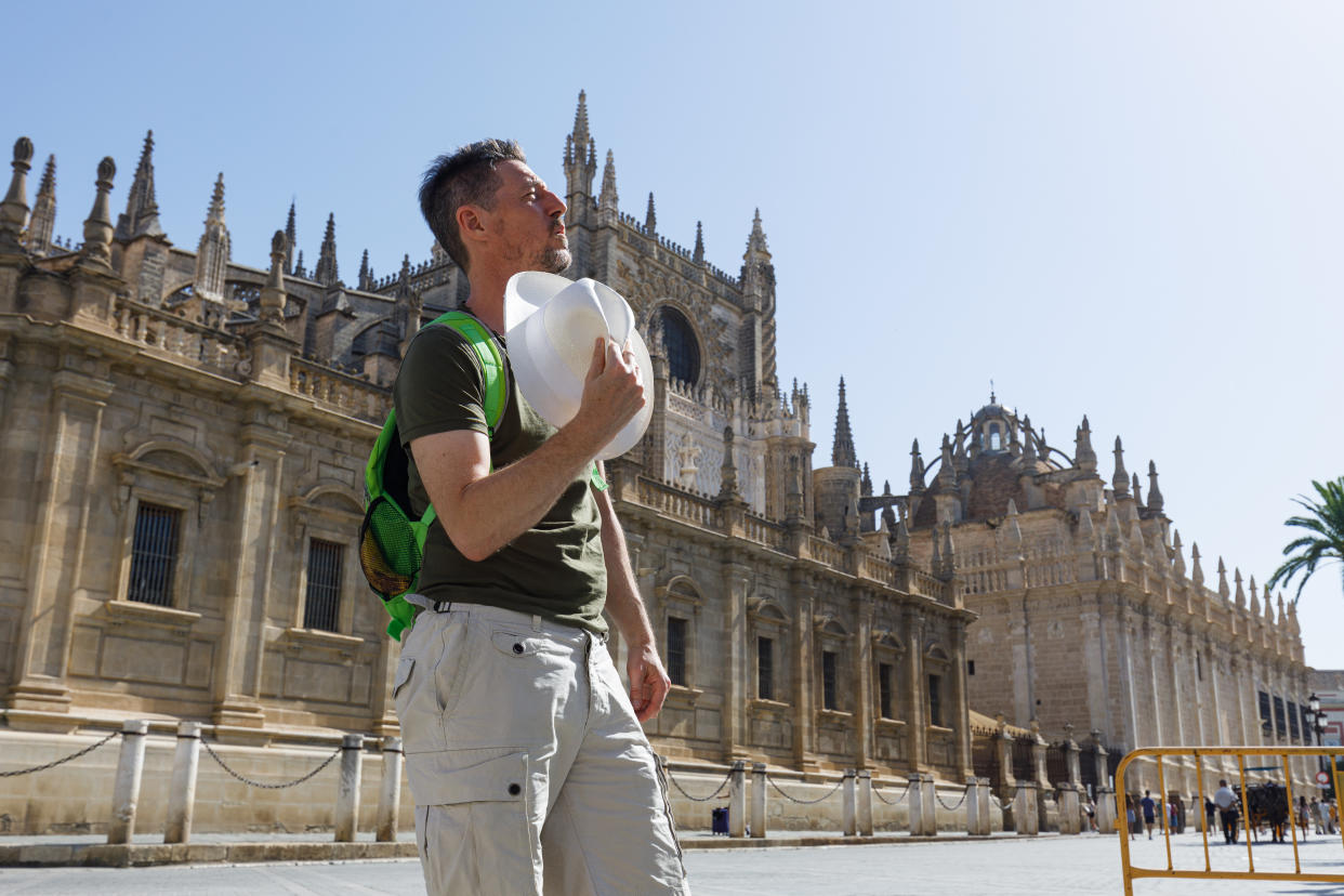 Mature man standing in front of cathedral in Seville, Spain. Cooling down with his hat.