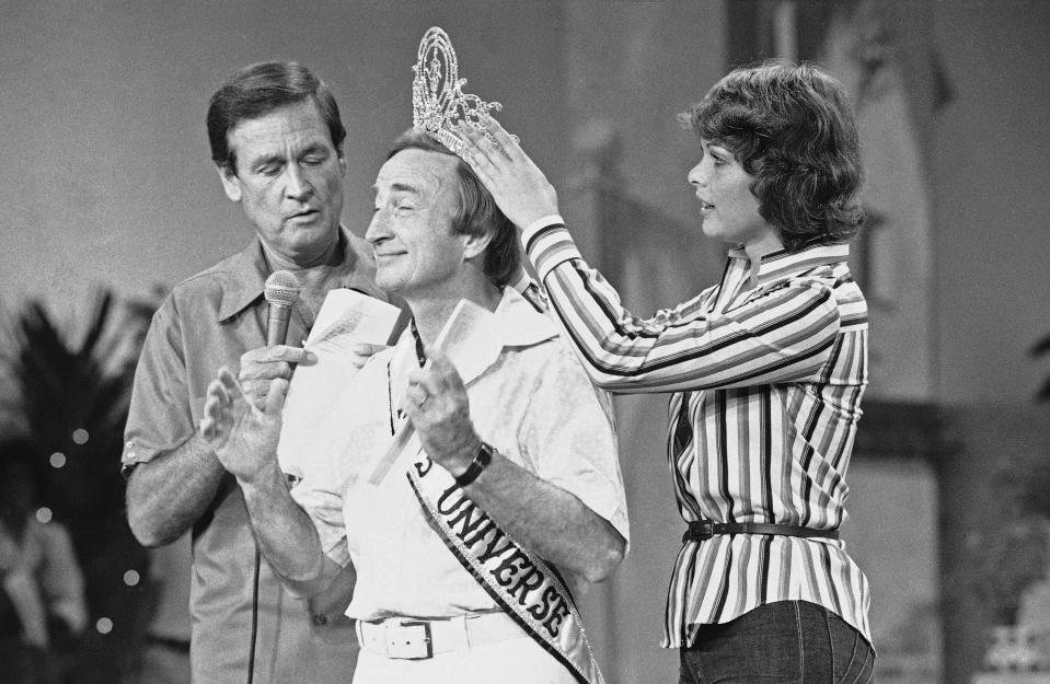 Gene Bayliss, choreographer for the Miss Universe pageant, acts as a stand-in for the Miss Universe winner during rehearsal in Santo Domingo, Dominican Republic on July 16, 1977. Bayliss, who has been choreographer for the contest for 11 years, is crowned by the reigning Miss Universe Rina Messinger, right, as host Bob Barker looks on. (