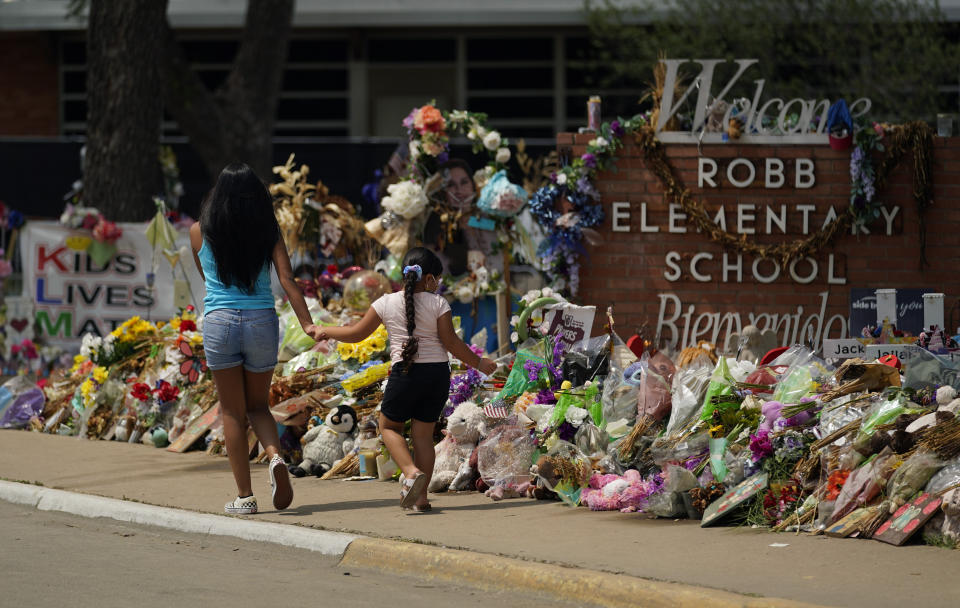 Visitors walk past a makeshift memorial honoring those recently killed at Robb Elementary School, Tuesday, July 12, 2022, in Uvalde, Texas. A Texas lawmaker says surveillance video from the school hallway where police waited as a gunman opened fire in a fourth-grade classroom will be shown this weekend to residents of Uvalde. (AP Photo/Eric Gay)