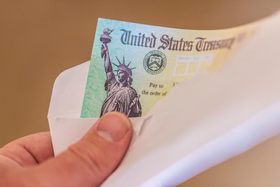 A person holding an envelope containing a check from the United States Treasury.