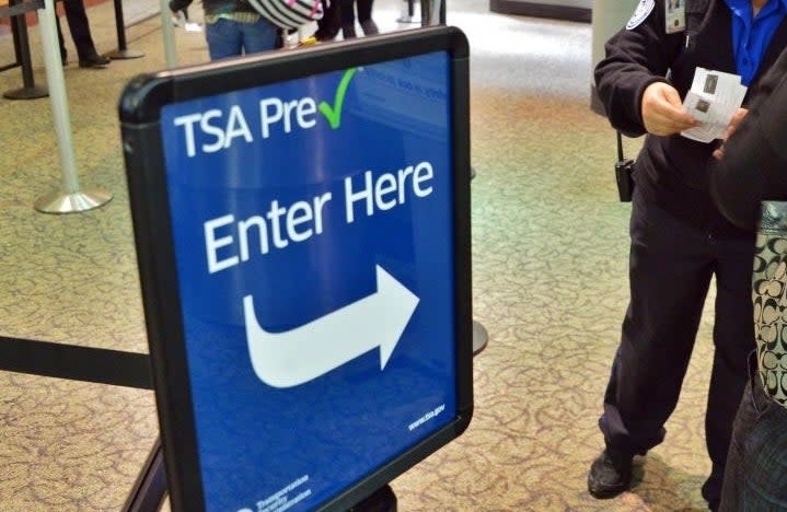 A TSA officer examines a passenger's documents in an airport's TSA PreCheck line, indicated by a sign that reads "TSA Pre✓ Enter Here."