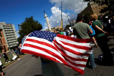 A woman carries an American flag while construction crew prepare a monument of Robert E. Lee, who was a general in the Confederate Army, for removal in New Orleans, Louisiana, U.S., May 19, 2017. REUTERS/Jonathan Bachman