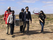 In this photo provided by the Australian Space Agency, members of the Japan Aerospace Exploration Agency (JAXA) arrive at a range support facility in Woomera, Australia, Sunday, Dec. 6, 2020, carrying a box containing asteroid samples that they retrieved on a remote area in southern Australia. JAXA said Hayabusa2 released the small capsule of samples Saturday. JAXA officials said they hoped to conduct a preliminary safety inspection at an Australian lab and bring the capsule back to Japan soon. (Australian Space Agency via AP)