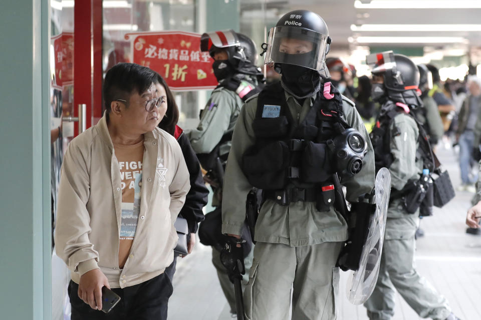 A man walks past riot police at a shopping mall popular with traders from mainland China near the Chinese border in Hong Kong, Saturday, Dec. 28, 2019. Protesters shouting "Liberate Hong Kong!" marched through a shopping mall Saturday to demand that mainland Chinese traders leave the territory in a fresh weekend of anti-government tension. (AP Photo/Lee Jin-man)