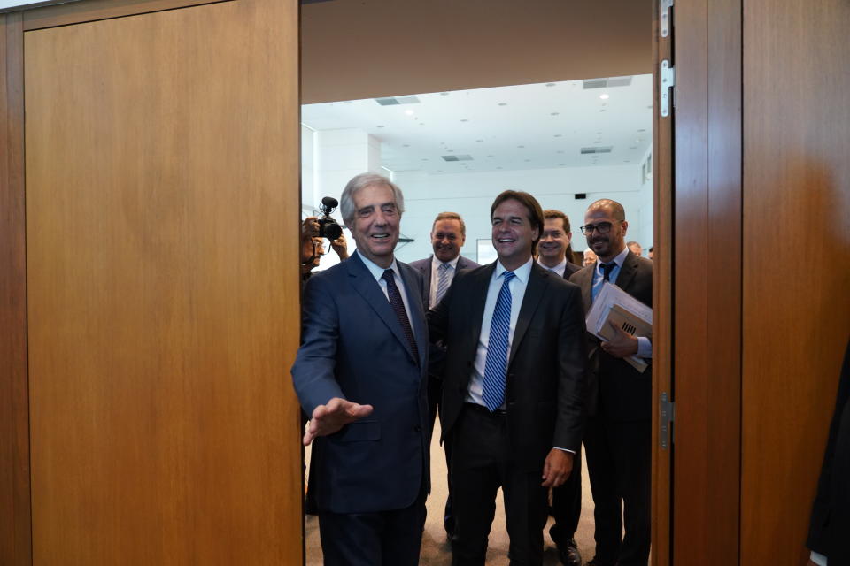 El presidente de Uruguay, Tabaré Vázquez, a la izquierda, es sorprendido por la prensa después de abrir una puerta mientras recorre las oficinas presidenciales junto al presidente electo Luis Lacalle Pou en el centro de Montevideo, Uruguay, el lunes 2 de diciembre de 2019. (AP Foto / Matilde Campodonico)