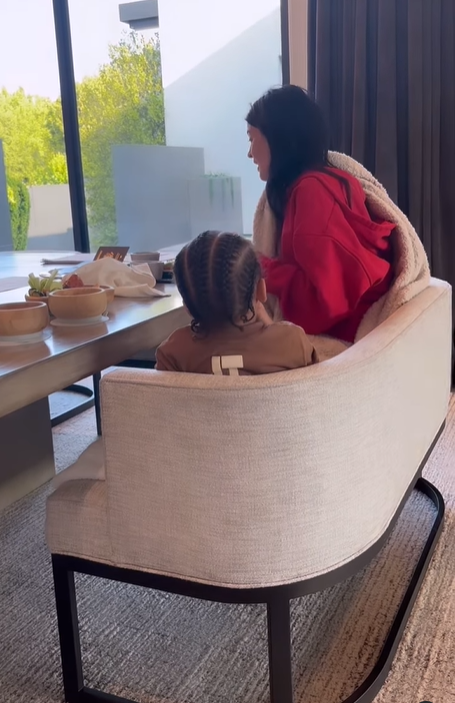 Kylie Jenner and her son Aire sat on a beige dining sofa a black metal frame