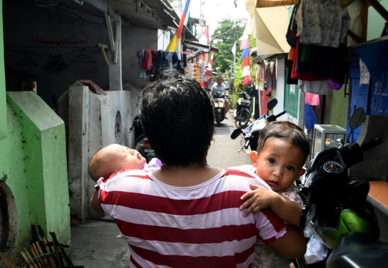 An Indonesian woman carries her children along the neighbourhood where Dedy Sukma, who Indonesian police accused of stealing a motorcycle before he was shot and killed, used to live in Jakarta