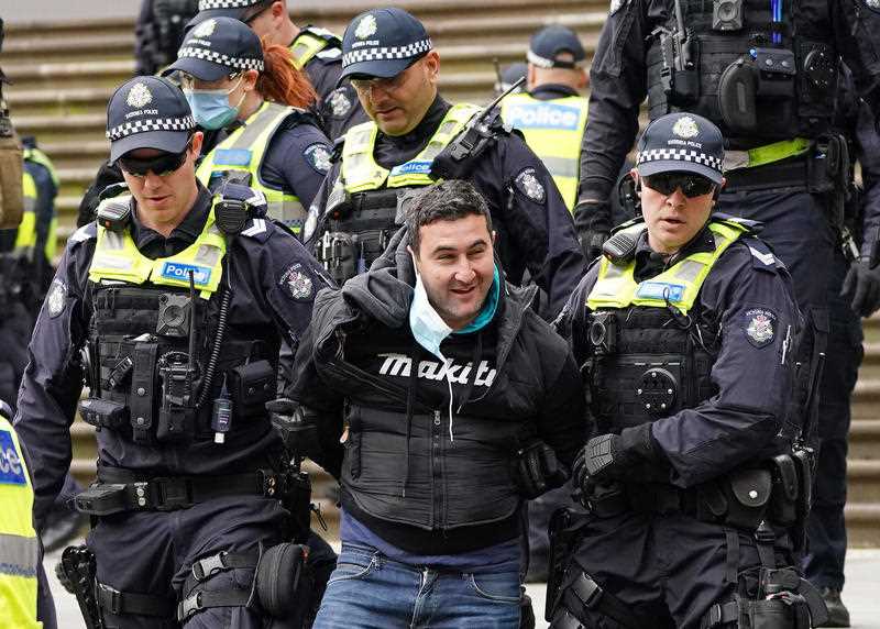 Police officers detain a man as protesters gather outside Parliament House in Melbourne.