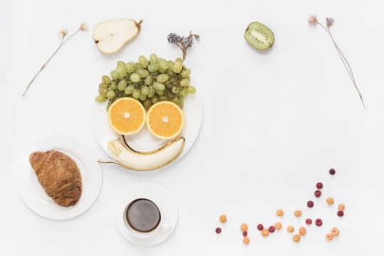 Face made of banana, oranges, and grapes on a plate for kids