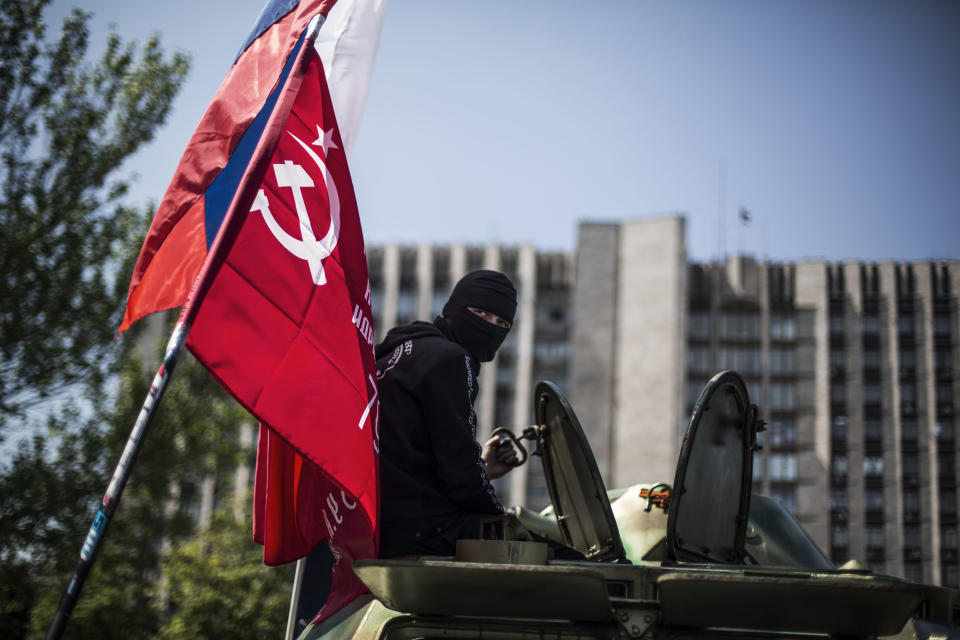 A masked pro Russia man is seen atop an APC flying a Russian flag, top, and a Donetsk People's Republic flag, as it stands in front of the occupied administration building in Donetsk, Ukraine, Saturday, May 10, 2014. Two restive regions in eastern Ukraine are preparing to vote on declaring sovereignty and ceding from Ukraine, in a referendum on Sunday in the Donetsk and Luhansk regions, where pro-Russia insurgents have seized government buildings and clashed with police and Ukrainian troops.(AP Photo/Manu Brabo)