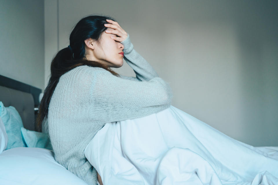 A young woman is sitting in bed looking distressed