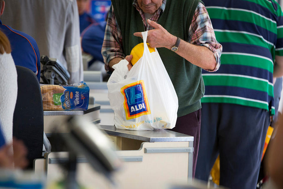 A customer places a melon into a plastic carrier bag, branded with the Aldi name. Source: Getty