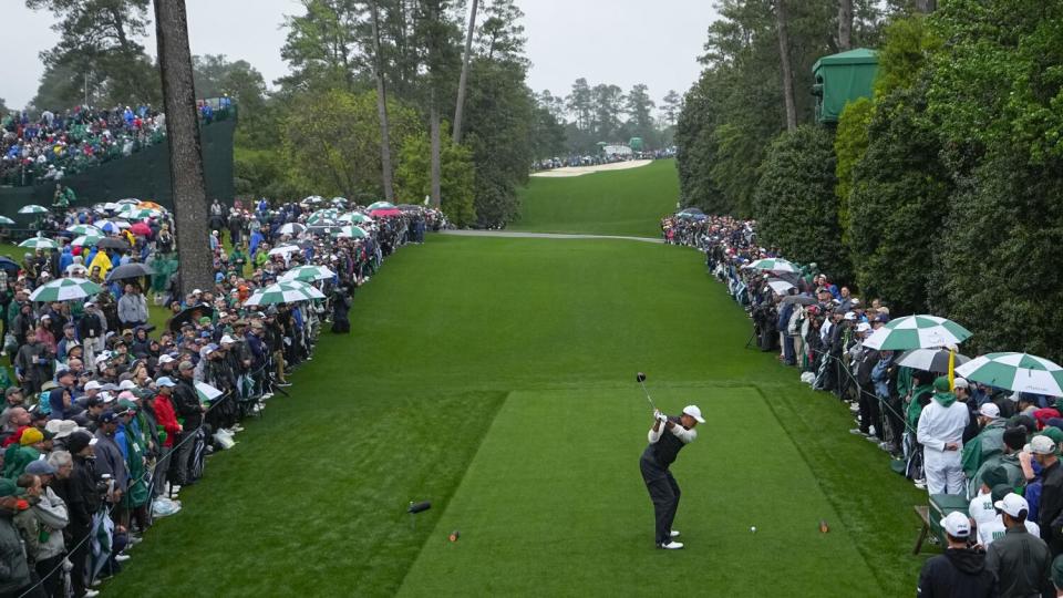 Tiger Woods hits from the 18th tee while onlookers watch on either side of him.