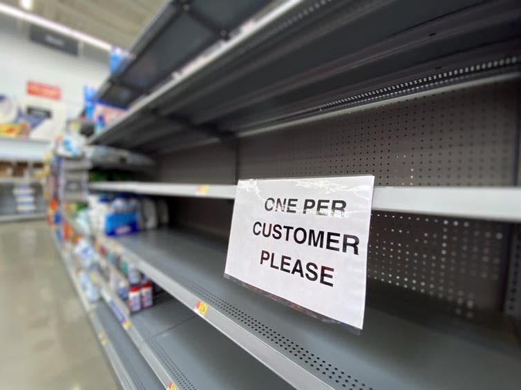Empty supermarket shelf with 'one per customer' sign