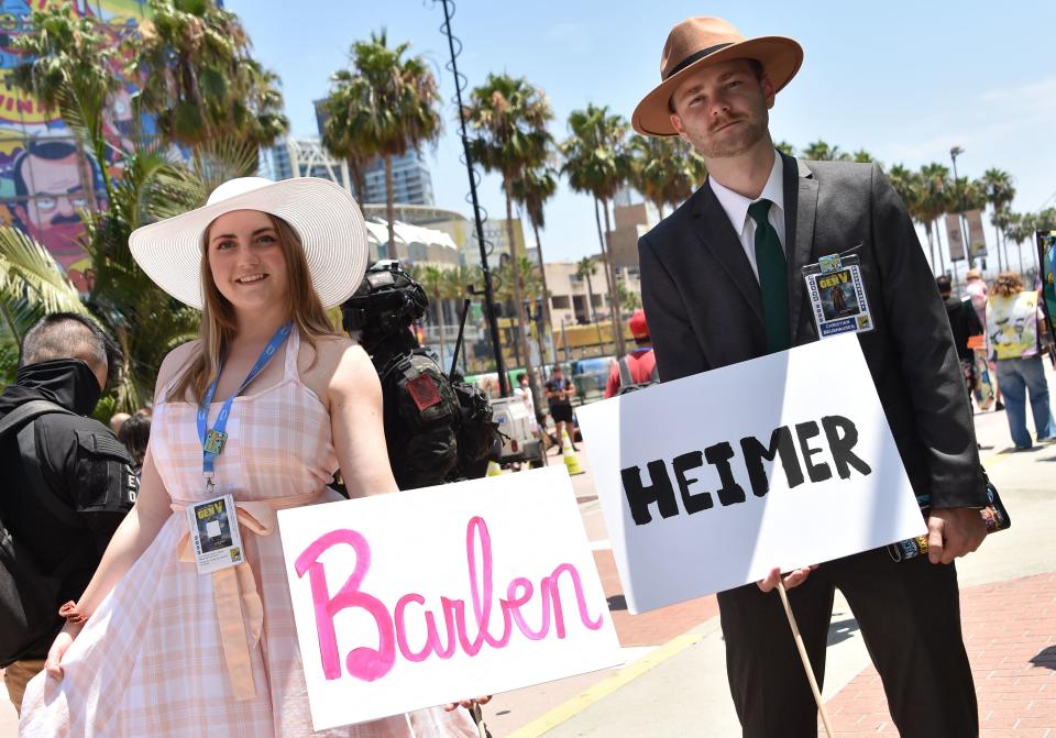 Cosplayers hold Barbenheimer signs outside the convention center during San Diego Comic-Con