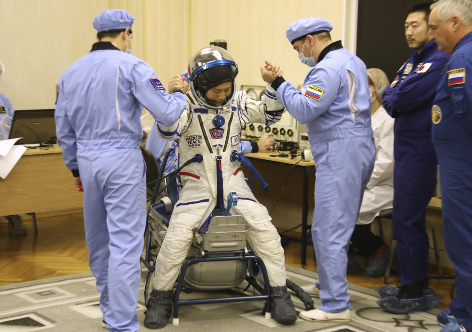 In this photo released by the Roscosmos Space Agency, Russian Space Agency experts help spaceflight participant Yusaku Maezawa of Japan, member of the main crew of the new Soyuz mission to the International Space Station (ISS) to stand up after inspecting his space suit prior to the launch at the Russian leased Baikonur cosmodrome, Kazakhstan, Wednesday, Dec. 8, 2021. (Pavel Kassin/Roscosmos Space Agency via AP)