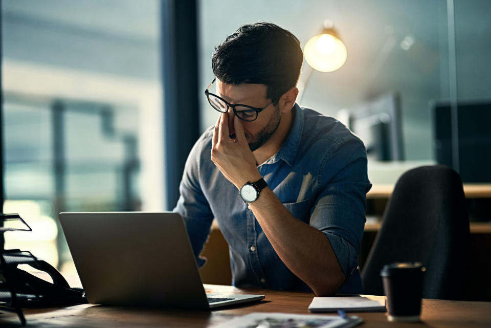 A man rubbing his eyes and sitting at a laptop