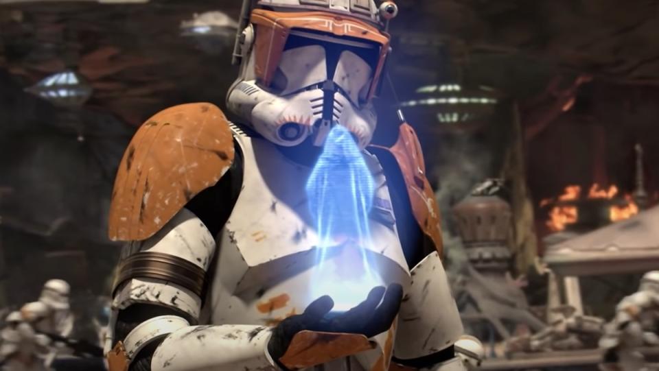 A clone trooper with white and orange gear looks at a hologram of Emperor Palpatine as a battle rages on behind him