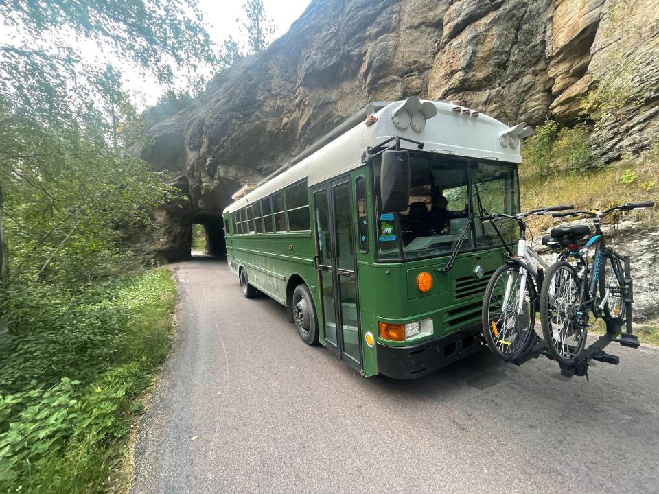 School bus on road with carved out tunnel on side of mountain in background