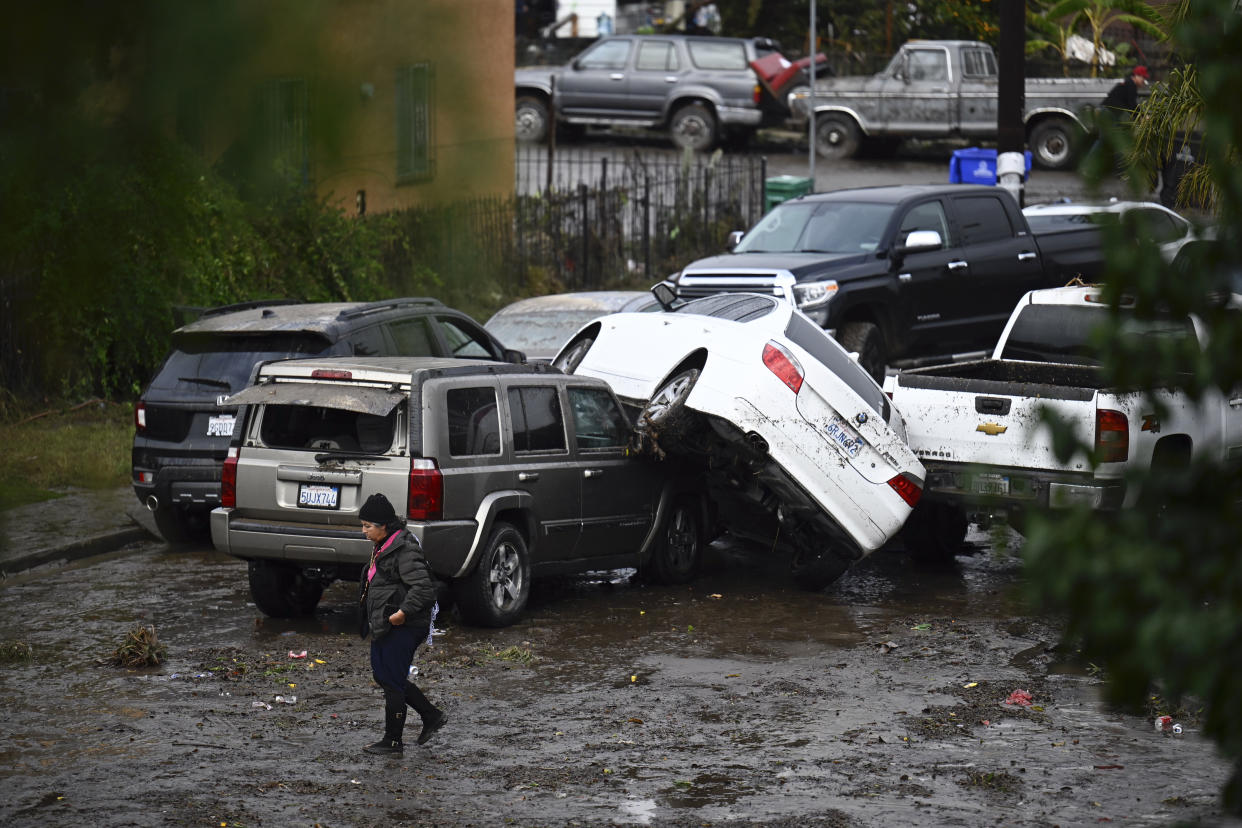 A woman walks by cars damaged by floods during a rainstorm in San Diego on Monday, Jan. 22, 2024. (AP Photo/Denis Poroy)