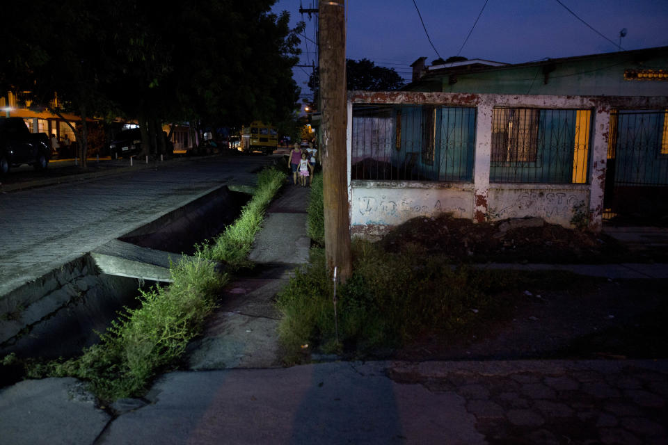 In this Oct. 30, 2018 photo, residents walk on a sidewalk in the Ciudad Planeta neighborhood of San Pedro Sula, Honduras. Ciudad Planeta looks like an ordinary working-class neighborhood, with one-story concrete houses with metal roofs, but in fact it is one of the most dangerous neighborhoods in one of the world's most dangerous countries. (AP Photo/Moises Castillo)