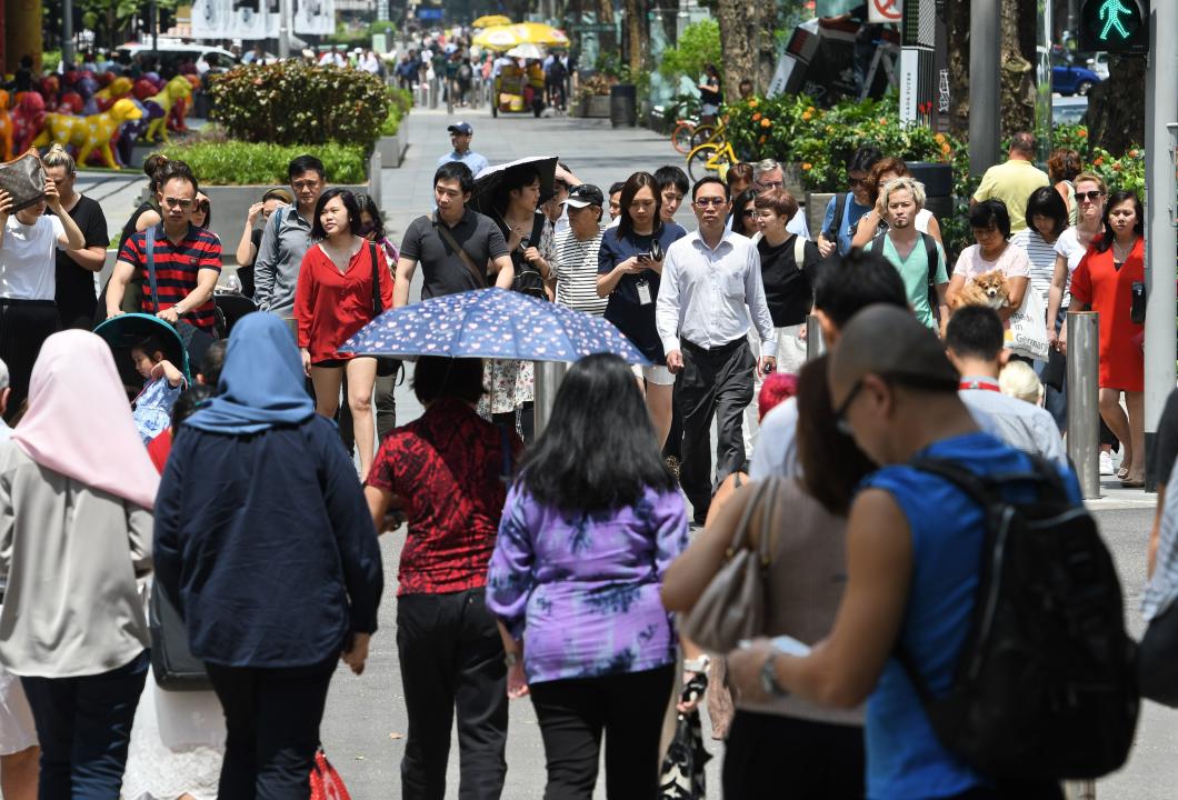 Pedestrians wait to cross the street along the Orchard Road shopping district in Singapore on February 21, 2018. / AFP PHOTO / Roslan RAHMAN        (Photo credit should read ROSLAN RAHMAN/AFP via Getty Images)