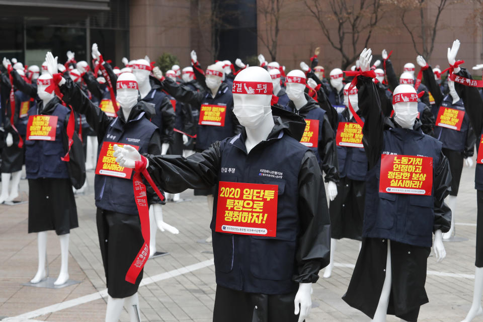 Mannequins are displayed as members of the KEB Hana Bank union stage a rally against their company's management policy in front of the bank's headquarters in Seoul, South Korea, Friday, March 12, 2021. The mannequins were used to avoid the violation of an ongoing ban on rallies with more than 10 people amid the coronavirus pandemic. The signs read: "Let's win wages through struggle, unity and fight." (AP Photo/Ahn Young-joon)