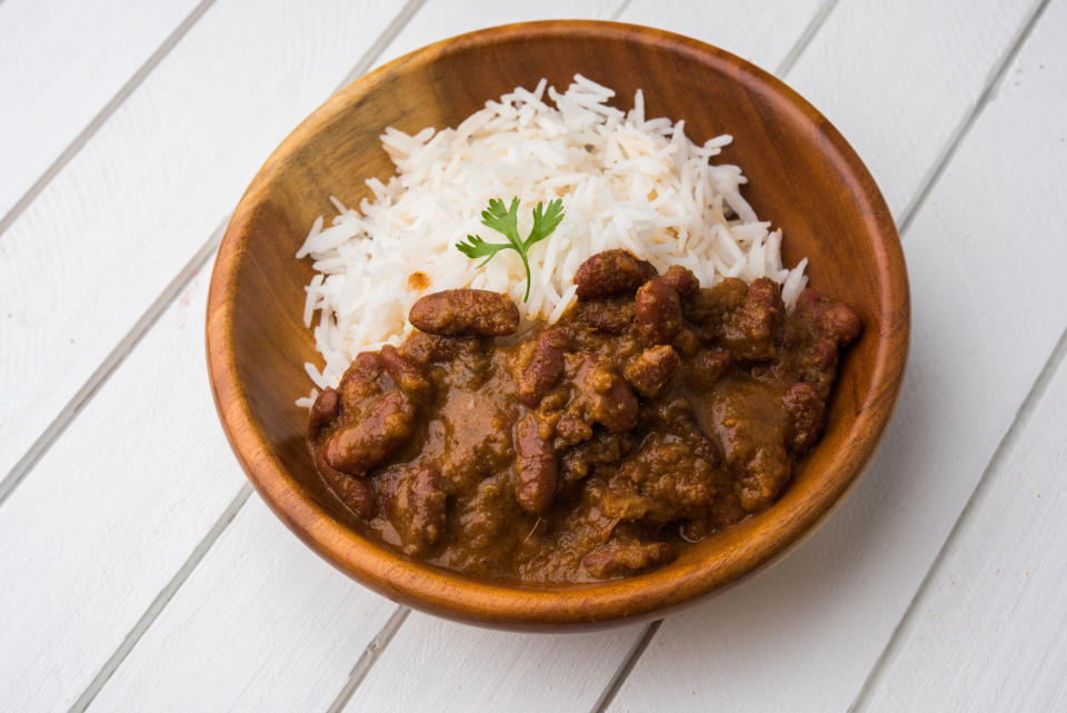 A bowl of rajma or kidney bean curry served with a side of basmati rice, garnished with a sprig of coriander