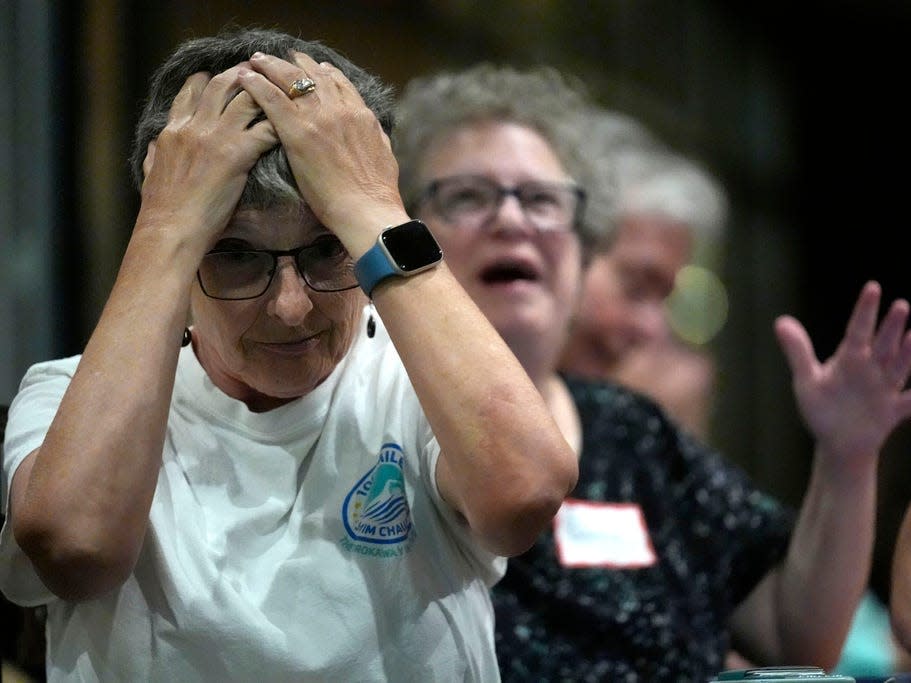 Two women with pained expressions, one with her hands on her head and another with her mouth open in shock.