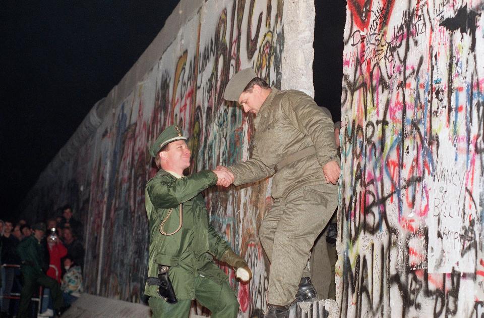 A West German policeman, left, gives a helping hand to an East German border guard who climbs through a gap of the Berlin Wall when East Germany opened another passage at Potsdamer Platz in Berlin, Nov. 12, 1989. 