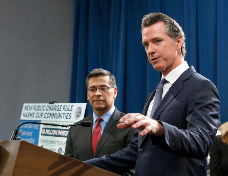 California Gov. Gavin Newsom, right, flanked by Attorney General Xavier Becerra, discusses the lawsuit the state has filed against the Trump administration's new rules blocking green cards for many immigrants who receive government assistance, during a news conference in Sacramento, Calif., Friday, Aug. 16, 2019.