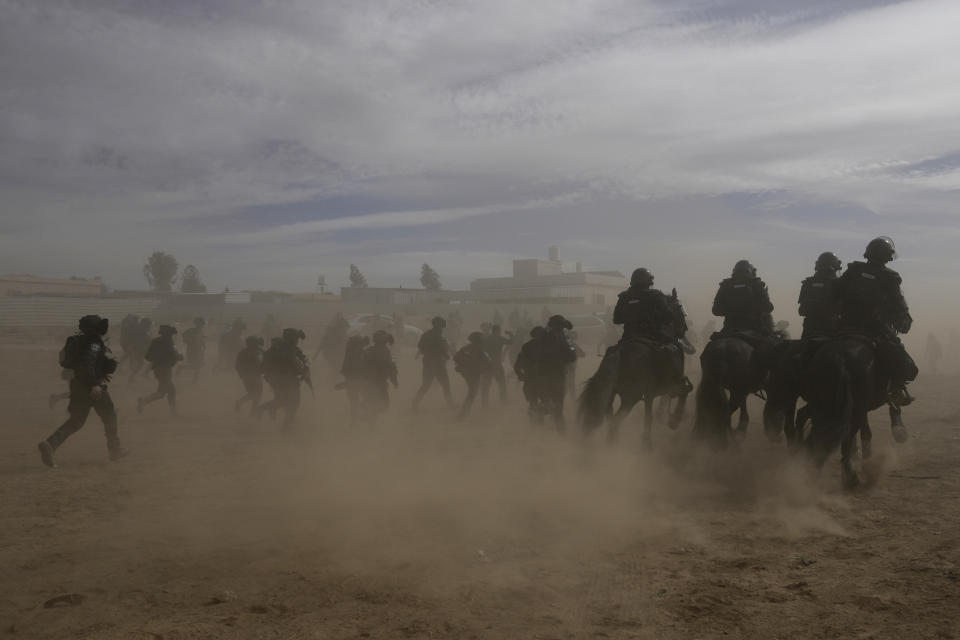 Israeli security forces advance during a protest held by Bedouins against tree-planting by the Jewish National Fund on disputed land near beduin village of al-Atrash at the Negev desert, southern Israel, Wednesday, Jan. 12, 2022. The conflict in southern Israel, which is home to Bedouin villages unrecognized by the state, has divided the Israeli government with Foreign Minister Yair Lapid calling for halting the tree-planting while the Islamist Ra'am party has threatened to withhold its votes in parliament in protest. (AP Photo/Mahmoud Illean)