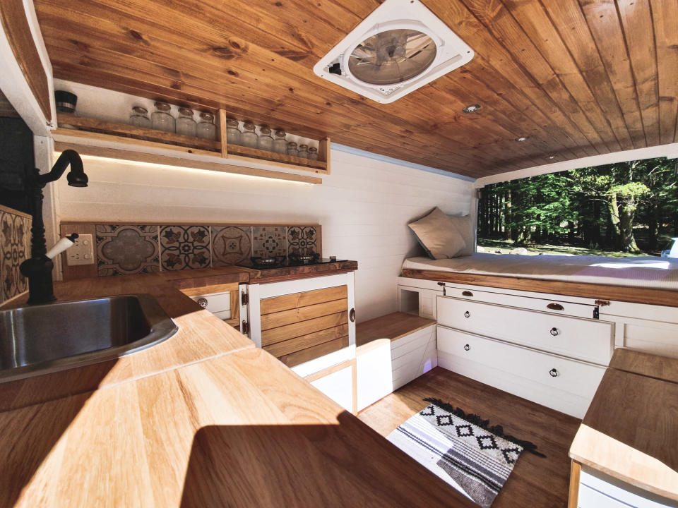 Interior of Sandy the Van shows wood and white panelling and kitchen with rug and green scene from window.