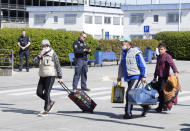 People arriving from Craiova in Romania walk past the police officers with their luggage and masks to a charter bus waiting at the 'Schoenefeld Airport' in Berlin, Germany, Thursday, April, 2020. The first planes with harvest workers from Romania have been landing in the morning. (Soeren Stache/dpa via AP)