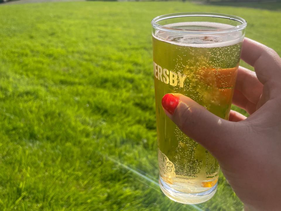 A woman's hand holding a glass of beer in a grassy area.