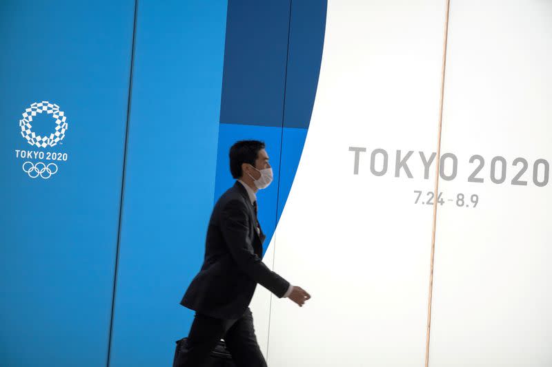 FILE PHOTO: A man wearing a protective face mask, following an outbreak of the coronavirus, walks past an advertising billboard of Tokyo Olympics 2020, near the Shinjuku station in Tokyo