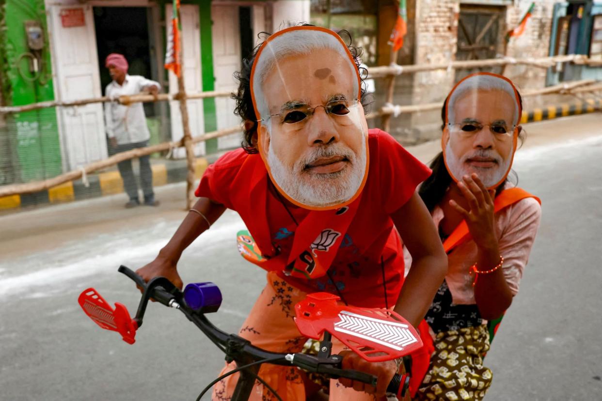 <span>Children wearing Narendra Modi masks ride a bicycle in Varanasi.</span><span>Photograph: Niharika Kulkarni/AFP/Getty Images</span>