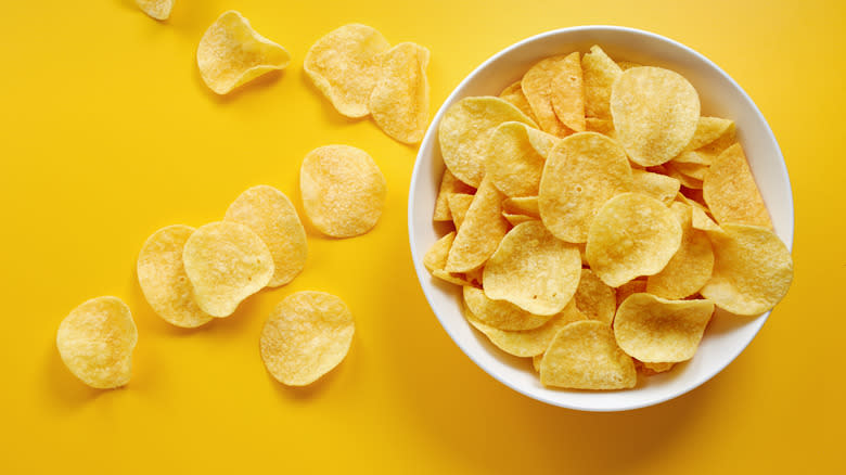 Potato chips in a bowl and on a yellow background