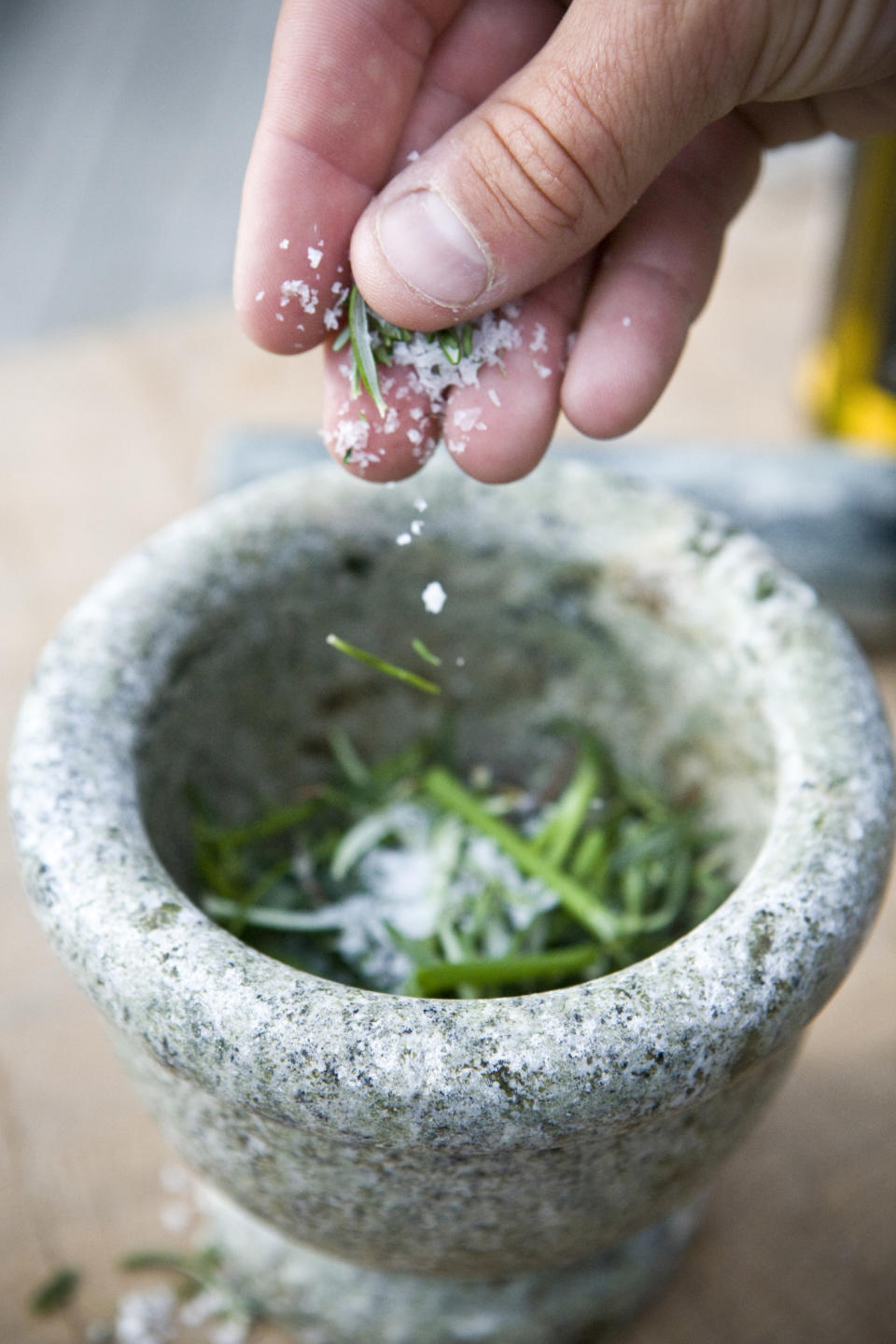 A hand putting salt on rosemary in a mortar