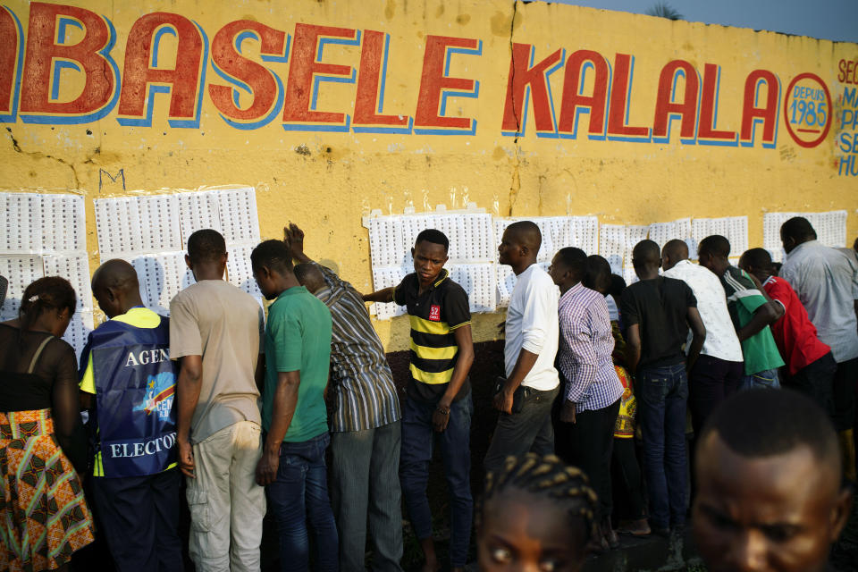 Election officials tape the voter's registrations list to the wall of the Les Anges primary school in Kinshasa, Congo, as voters start to check their names, Sunday Dec. 30, 2018. The voting process was delayed when angry voters burned six voting machines and ballots mid-day, angered by the fact that the registrations lists had not arrived. Replacement machines had to be brought in, and voting started at nightfall, 12 hours late. Forty million voters are registered for a presidential race plagued by years of delay and persistent rumors of lack of preparation. (AP Photo/Jerome Delay)