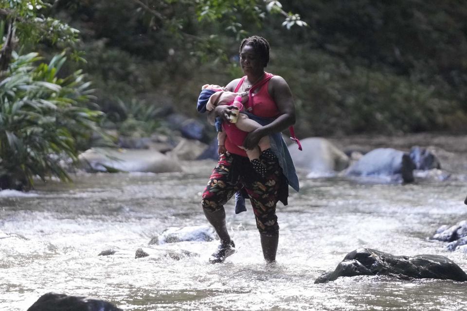 A migrant woman crosses the Acandi River with a child in her arms, in Acandi, Colombia, Wednesday, Sept. 15, 2021. A group of migrants, following a well-beaten, multi-nation journey towards the U.S., will continue their journey through a jungle known as the Darien Gap. (AP Photo/Fernando Vergara)