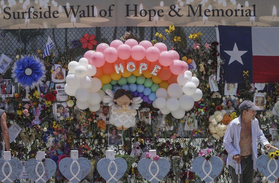 Wooden hearts with the names of victims are erected along side the photos, flowers, and other memorial items as visitors walk through the memorial site. 90 people have been confirmed dead due to the partial collapse of the Champlain Towers South in Surfside, Fla., on Sunday, July 11, 2021. (Carl Juste/Miami Herald via AP)