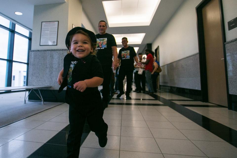 Aaron Morrison-Zinn, a 2-year-old from Lake Worth, laughs while running ahead of his soon-to-be adoptive parents Ted Zinn, center, and Mark Morrison, on the 11th floor of the Palm Beach County Courthouse on Friday, November 18, 2022, in downtown West Palm Beach, FL. Twenty-one children were adopted by families at National Adoption Day ceremonies at the Palm Beach County Courthouse.