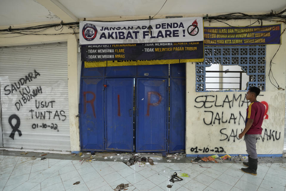 FILE - A man stands near a broken gate with graffiti "my brother was killed, investigate thoroughly," and "Good bye my brother" at Kanjuruhan Stadium where a deadly crush broke out on Saturday night, in Malang, Indonesia, Monday, Oct. 3, 2022. An Indonesian court began trial Monday, Jan. 16, 2023, against five men on charges of negligence leading to deaths of 135 people after police fired tear gas inside the stadium, setting off a panicked run for the exits in which many were crushed. (AP Photo/Achmad Ibrahim, File)