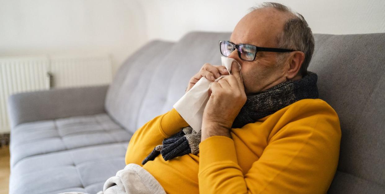 man blowing nose sitting on sofa at home