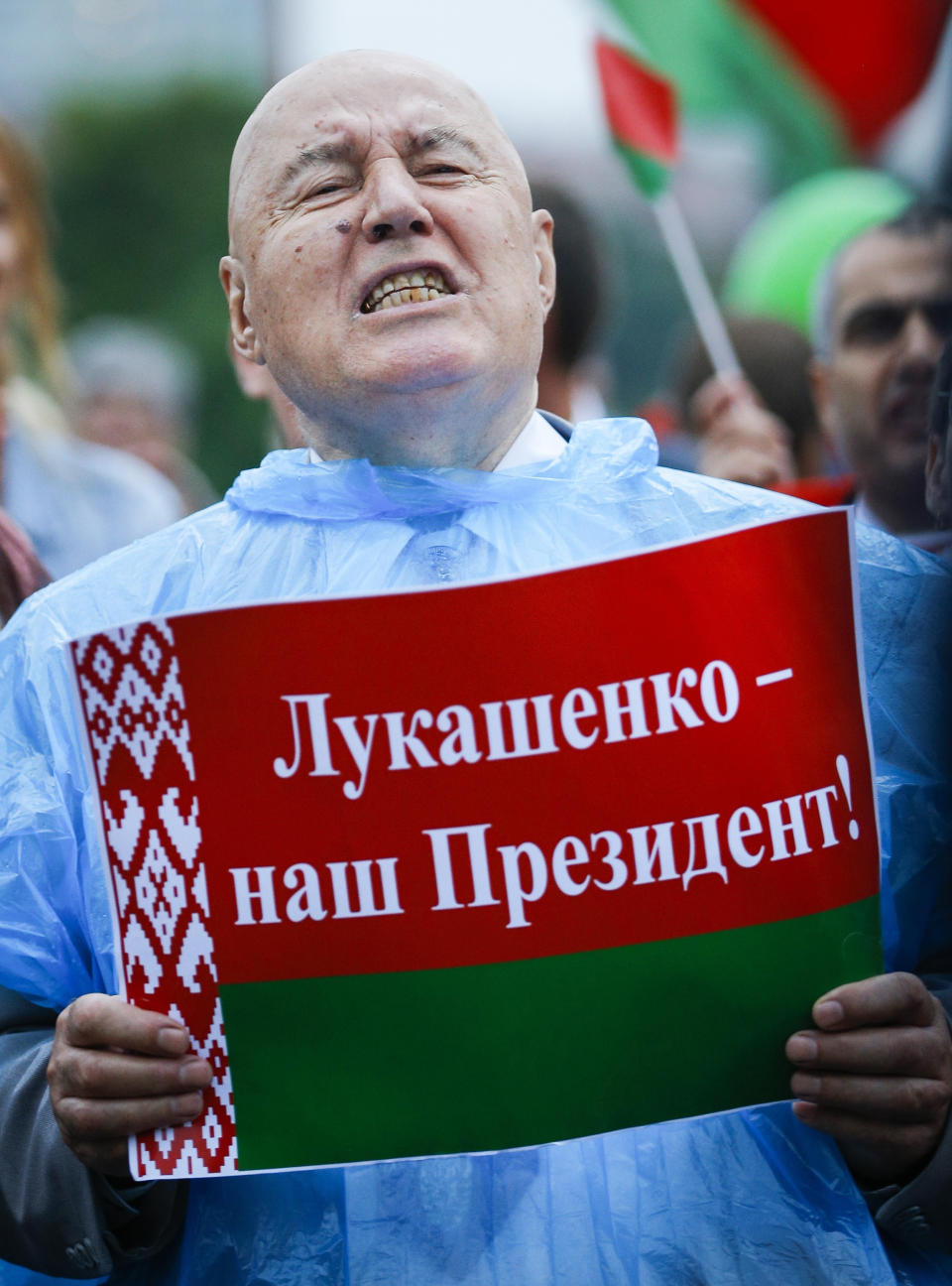 A man shouts holding a poster reads "Lukashenko is our President!" as other supporters of Belarusian President Alexander Lukashenko with Belarusian State flags gather in a square in Minsk, Belarus, Wednesday, Aug. 19, 2020. Belarus' authoritarian leader threatened Wednesday to take tough new steps against demonstrators challenging the extension of his 26-year rule and accused the West of fomenting unrest as he sought to consolidate his grip on power amid widening protests. (AP Photo/Sergei Grits)