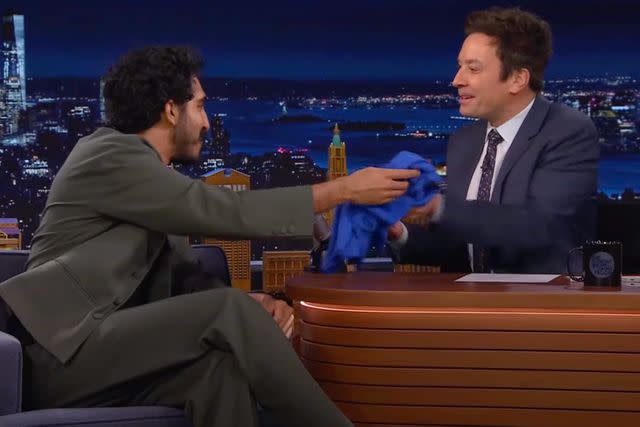 <p>YouTube/NBC</p> Dev Patel hands Jimmy Fallon a T-shirt with an X-ray of his broken hand